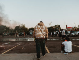 two men on a sidewalk overlooking a parking lot
