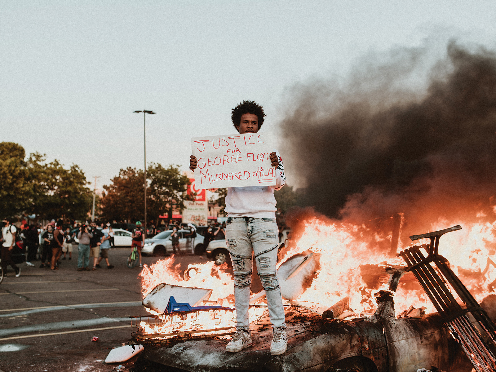 a man standing with a protest sign in front of a blazing fire