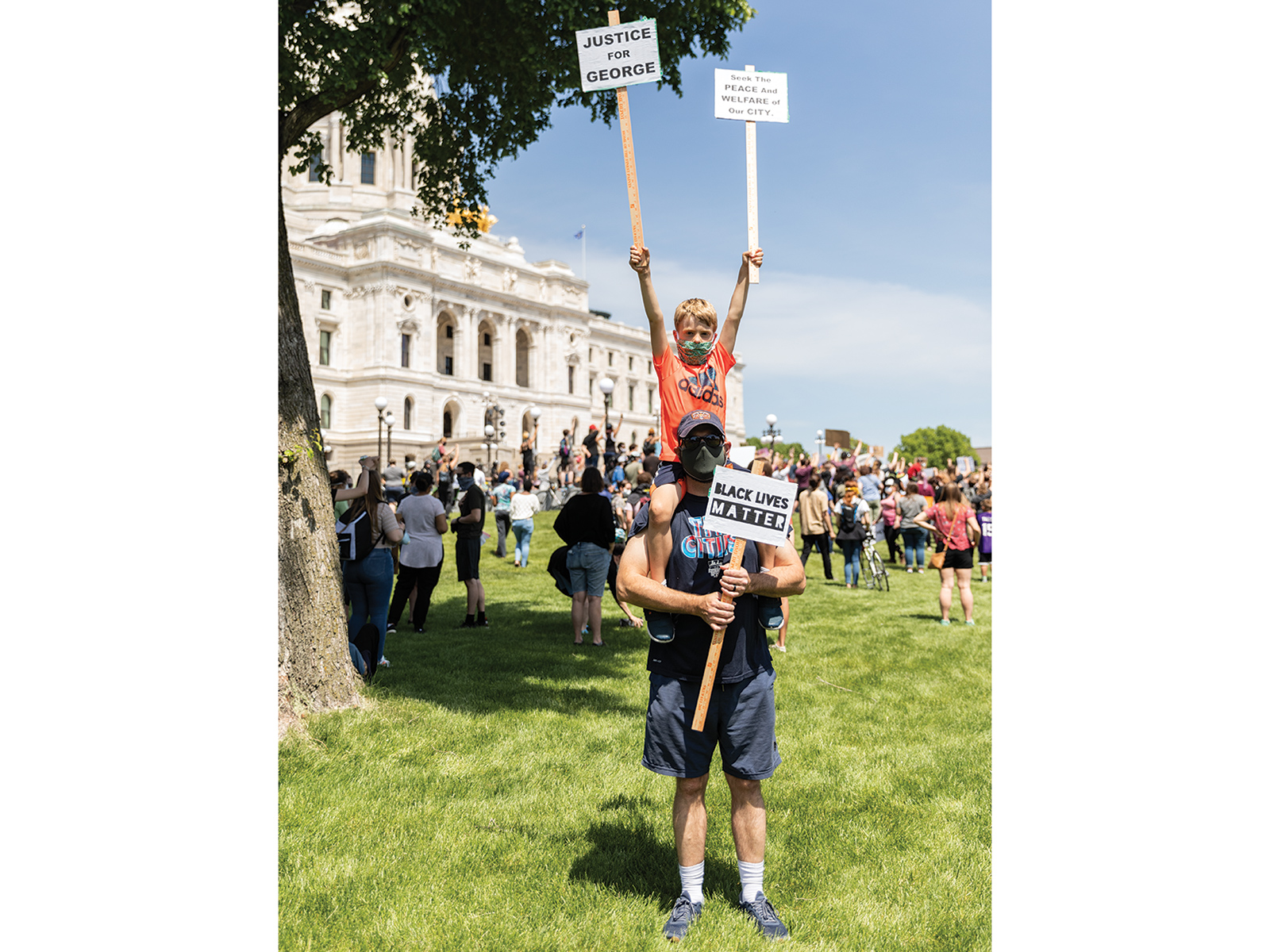 A child on the shoulders of his dad holding signs at a protest