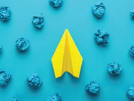 yellow paper airplane with crumpled up blue paper and blue background