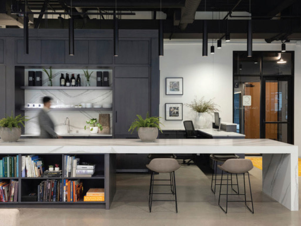 The central space features a reception area along with the 17-foot island, which serves as the core of the office. Toward the back is the kitchenette and through the paneled door is a “secret room” where printing and storage can be kept out of view.