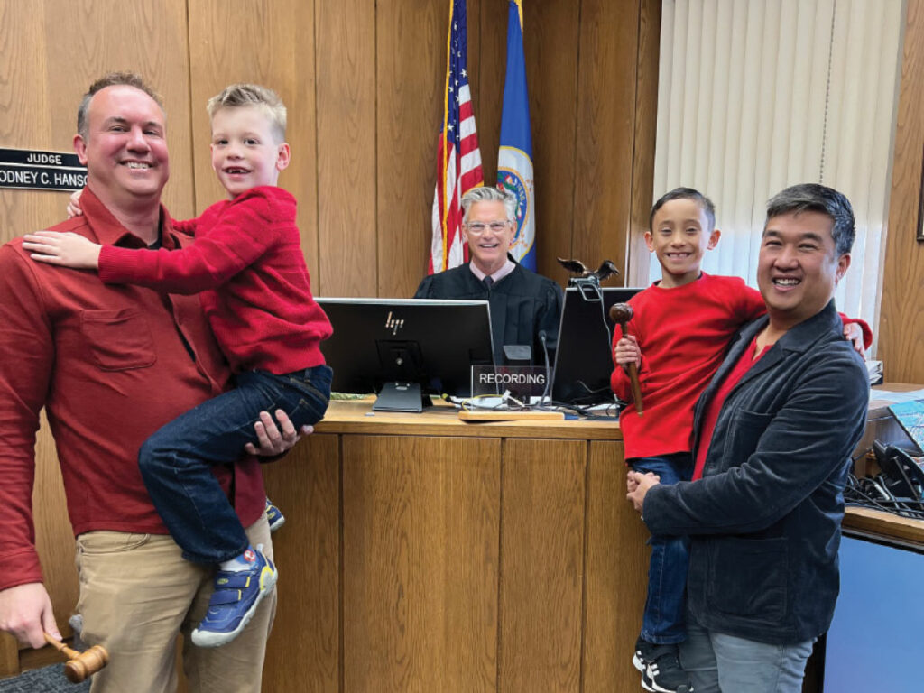two men pose with two children with a judge after adoption