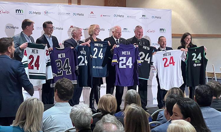 Gov. Tim Walz, flanked by local leaders and executives from Meta, hold jerseys with the company's name emblazoned on them.