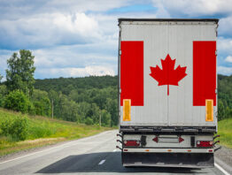 A truck with the national flag of Canada depicted on the back door carries goods to another country along the highway